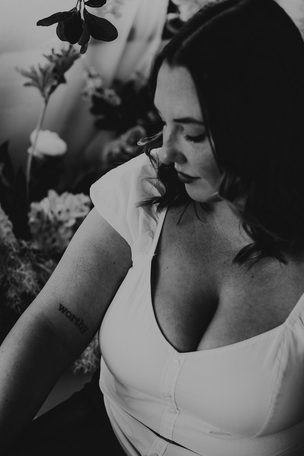 Artistic black and white portrait surrounded by soft floral elements and natural lighting.