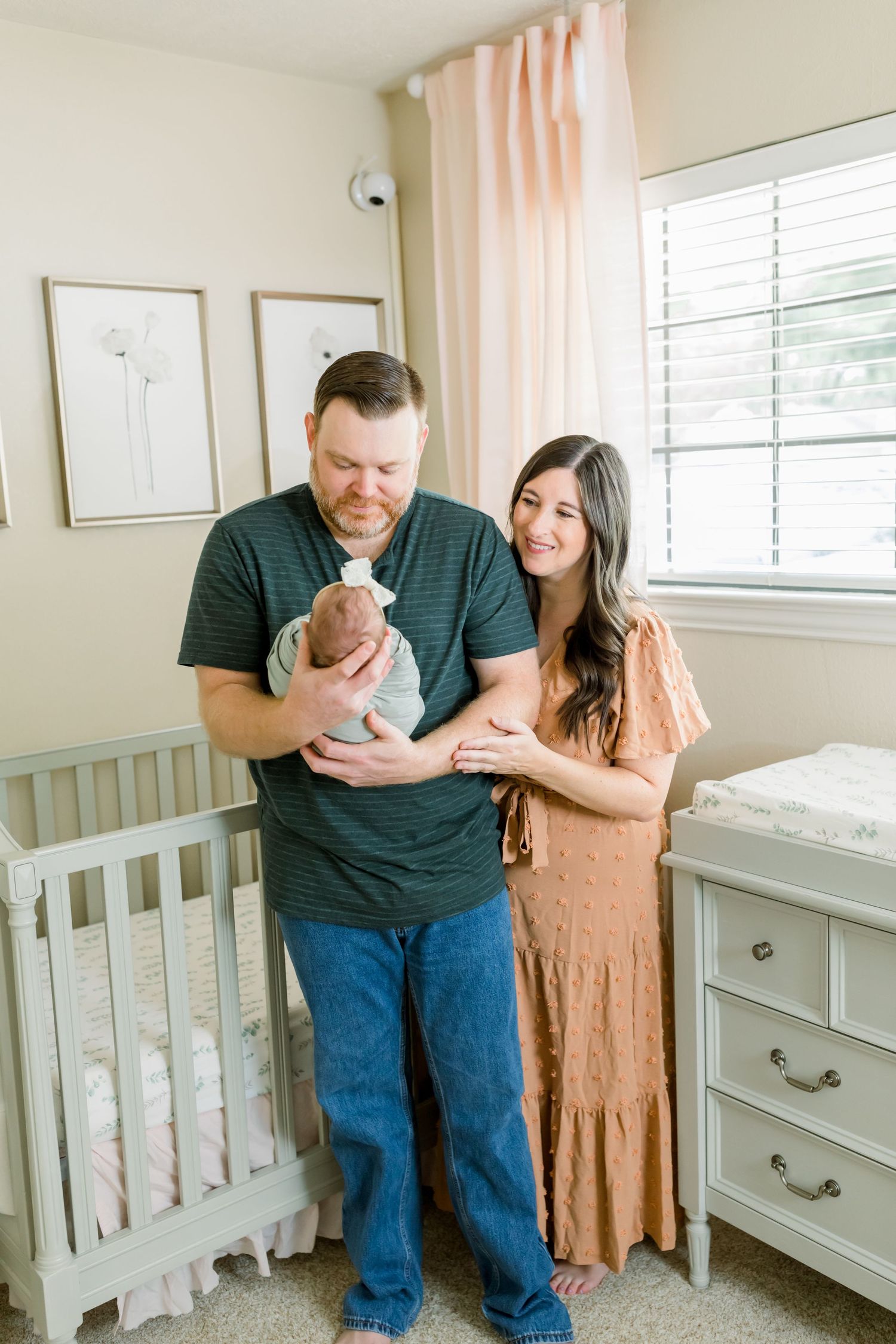 A couple gazes lovingly at their newborn baby in a nursery decorated with soft pink accents.