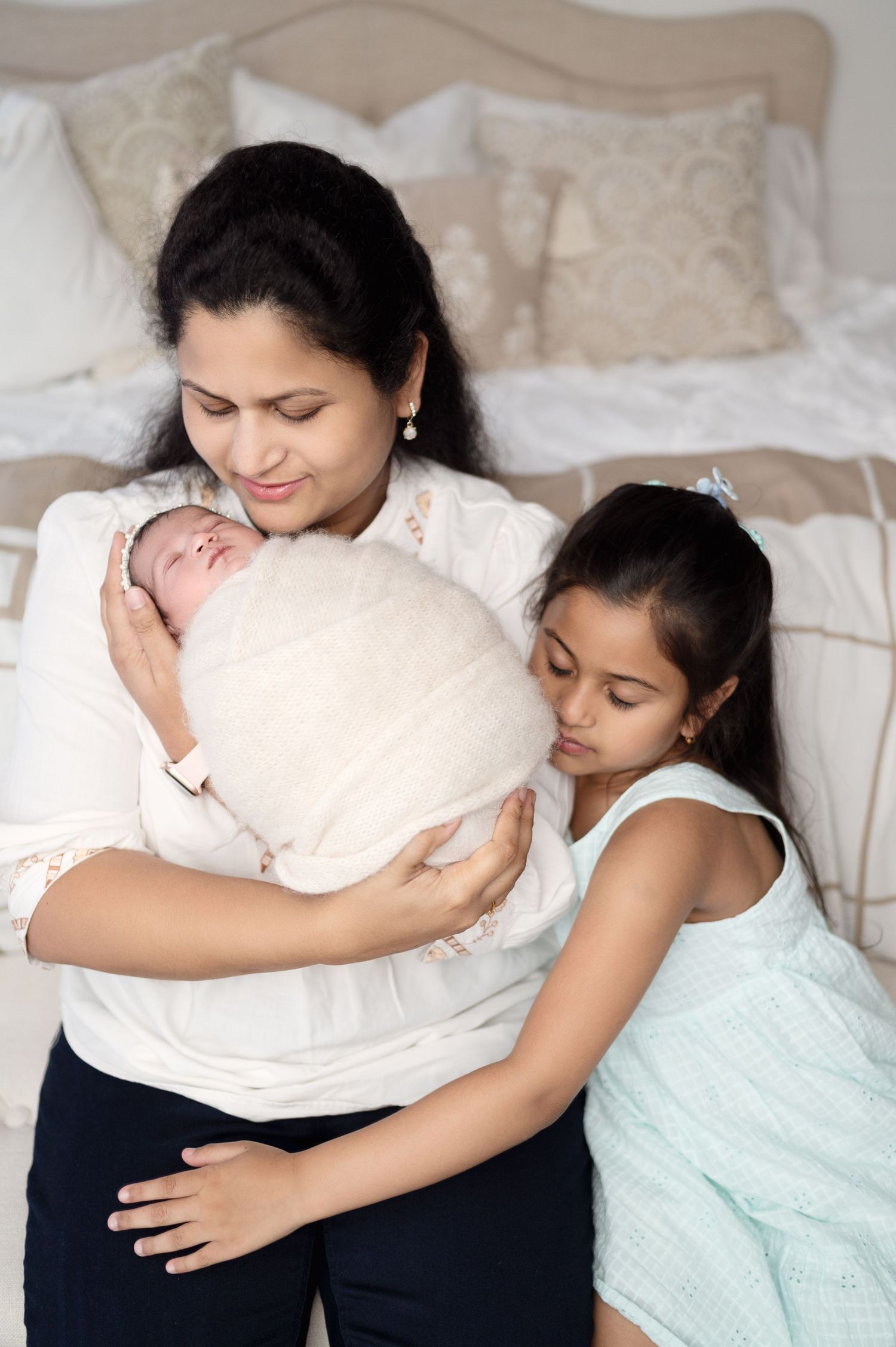 Mother and child share intimate moment with newborn baby swaddled in white.