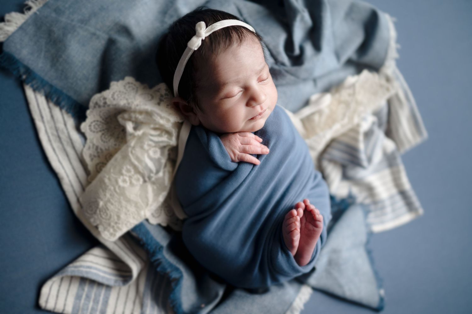 Artistic photo sequence of a sleeping newborn wrapped in cozy blue and white swaddle blankets.