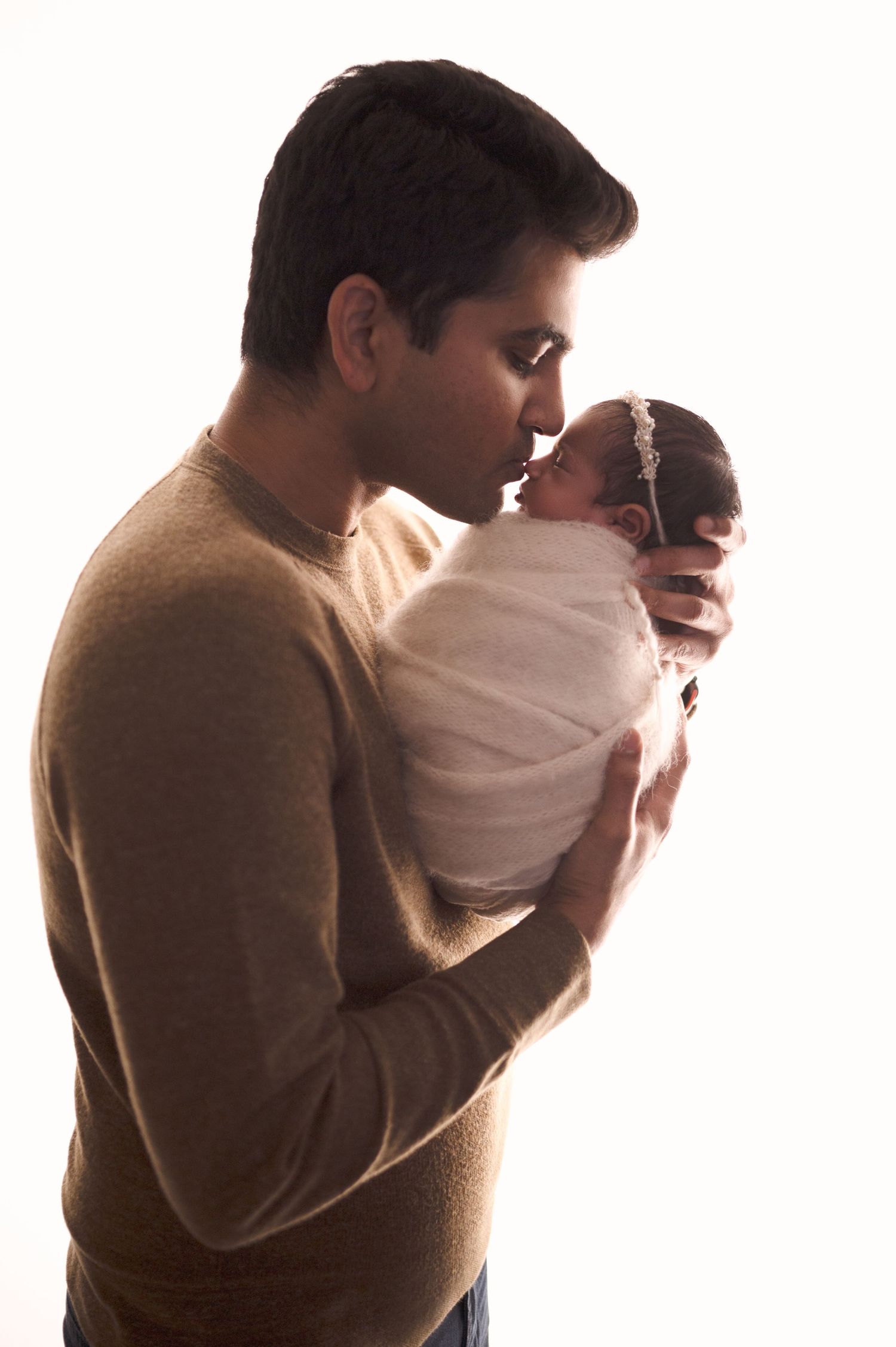 Side profile silhouette of parent holding swaddled baby in warm lighting.