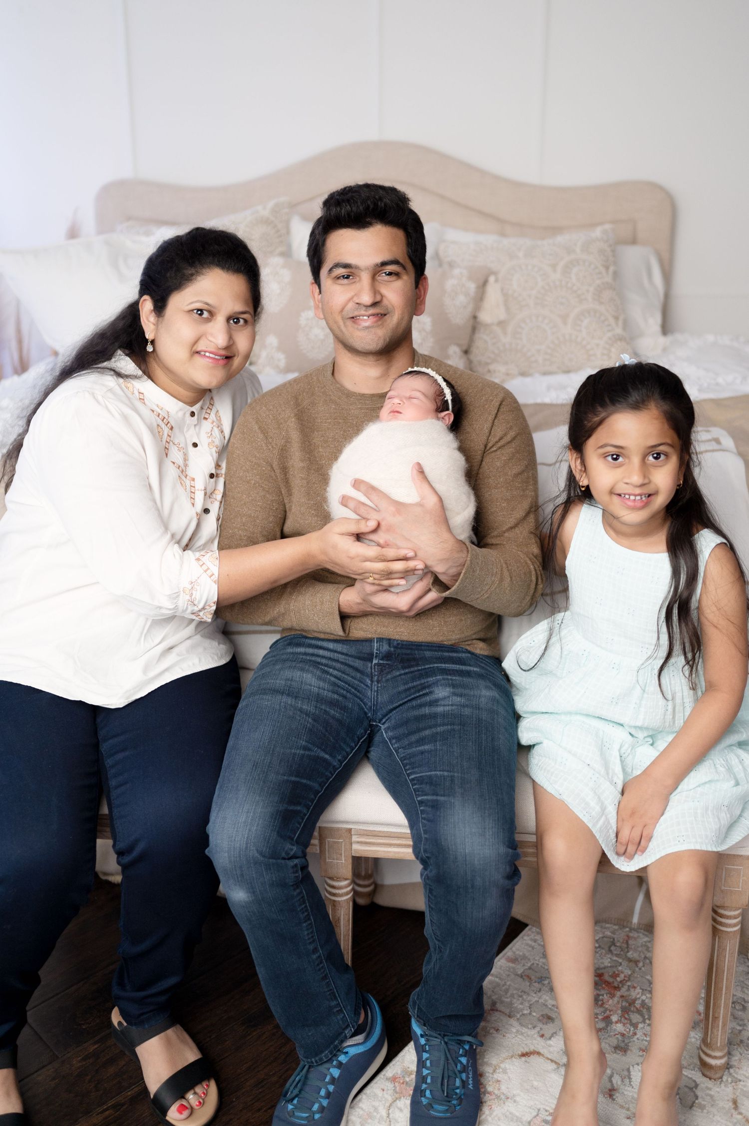 Family portrait with parents and young child sitting together on bed with newborn baby.