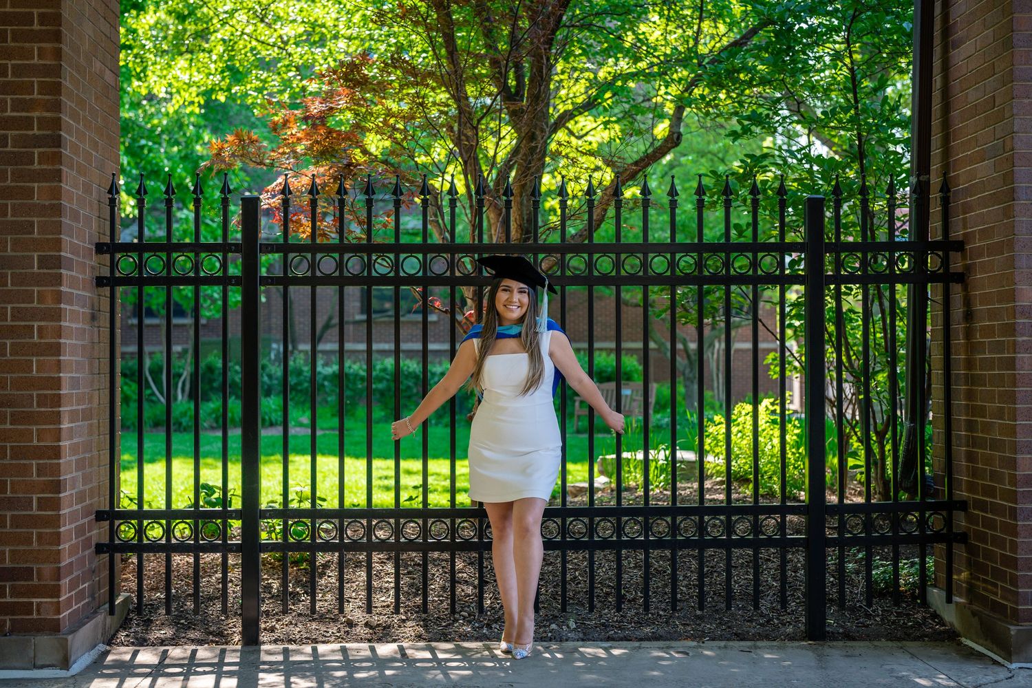 A scenic view through a brick archway showing an iron gate and lush green trees in the background.
