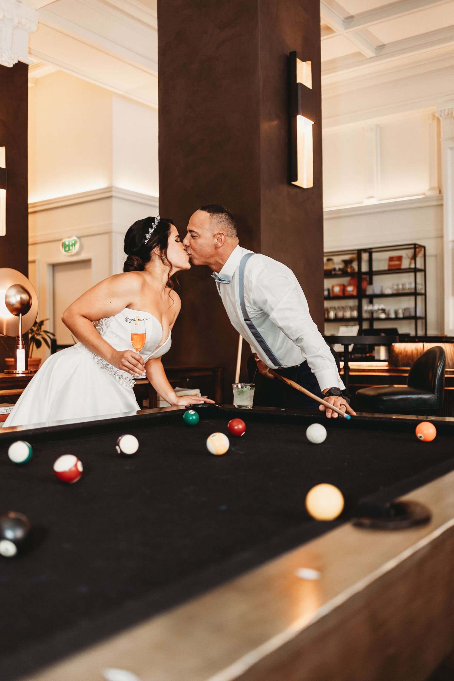 Wedding couple sharing a romantic kiss over a pool table in formal attire.