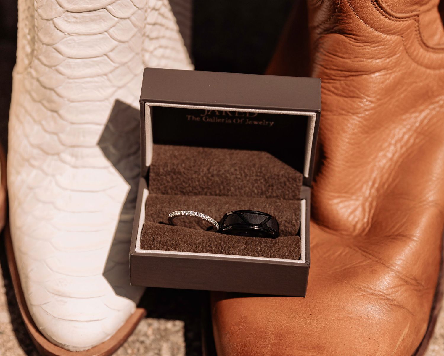 Wedding rings and jewelry displayed in elegant black boxes on a rustic wooden surface.