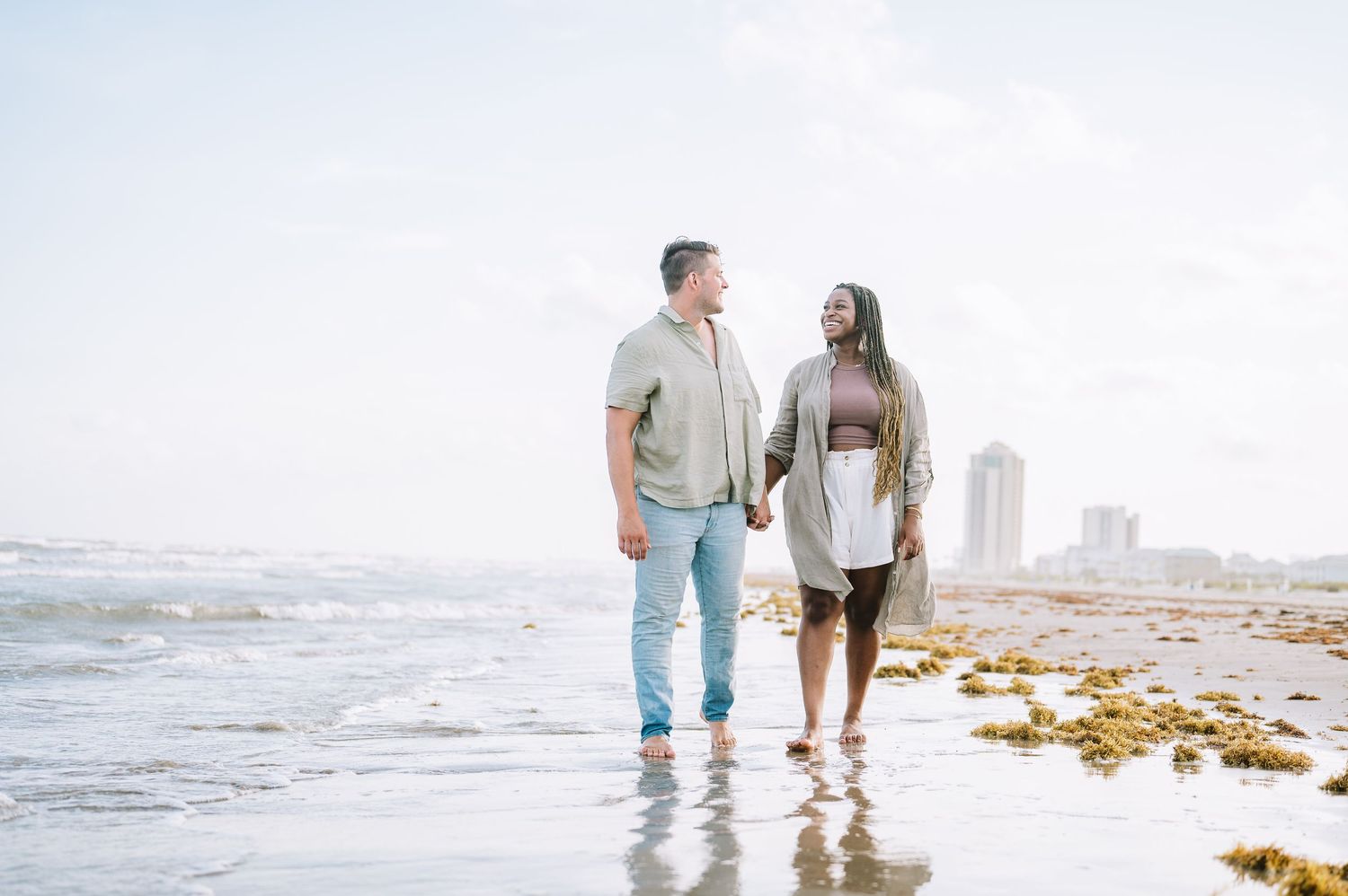 Romantic beach photoshoot with couple walking through shallow ocean water at golden hour.