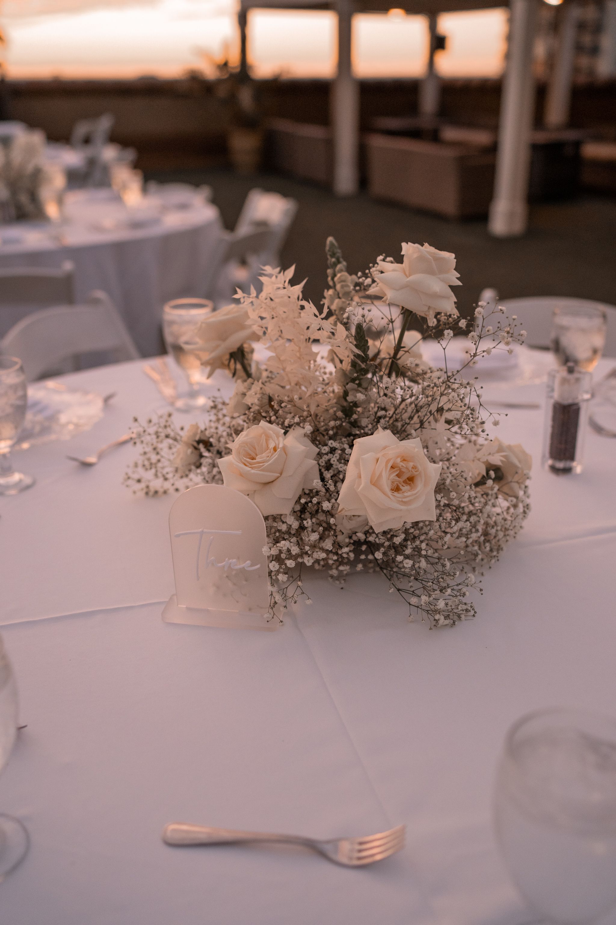 Elegant wedding centerpiece with white roses and baby's breath on a round table with white linens.