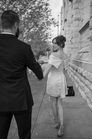 Elegant couple walking along stone building in formal attire.
