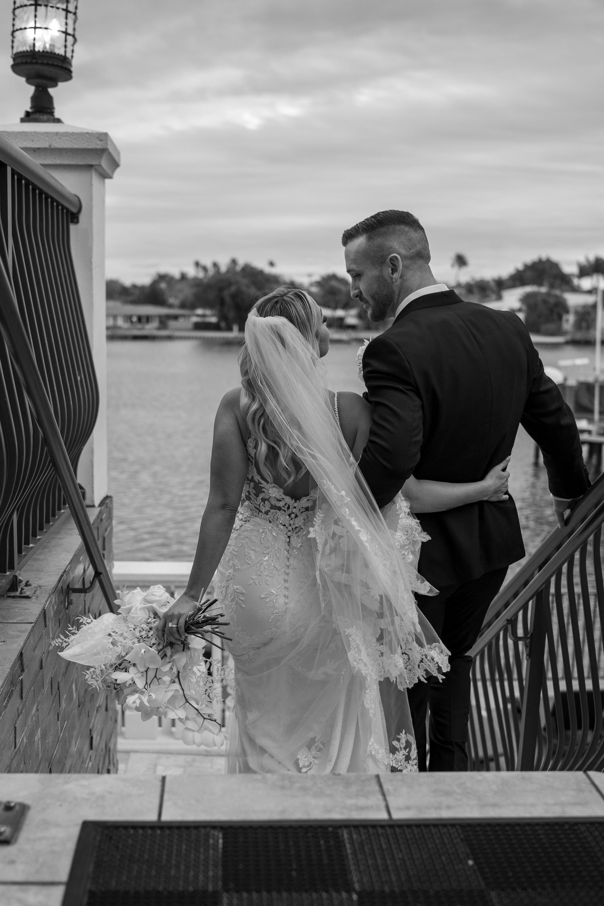 A wedding couple overlooking the waterfront from a decorated balcony.
