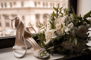 White bridal shoes and bouquet of roses arranged by window.