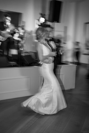 Motion-blurred black and white photo of bride dancing in fitted white gown.