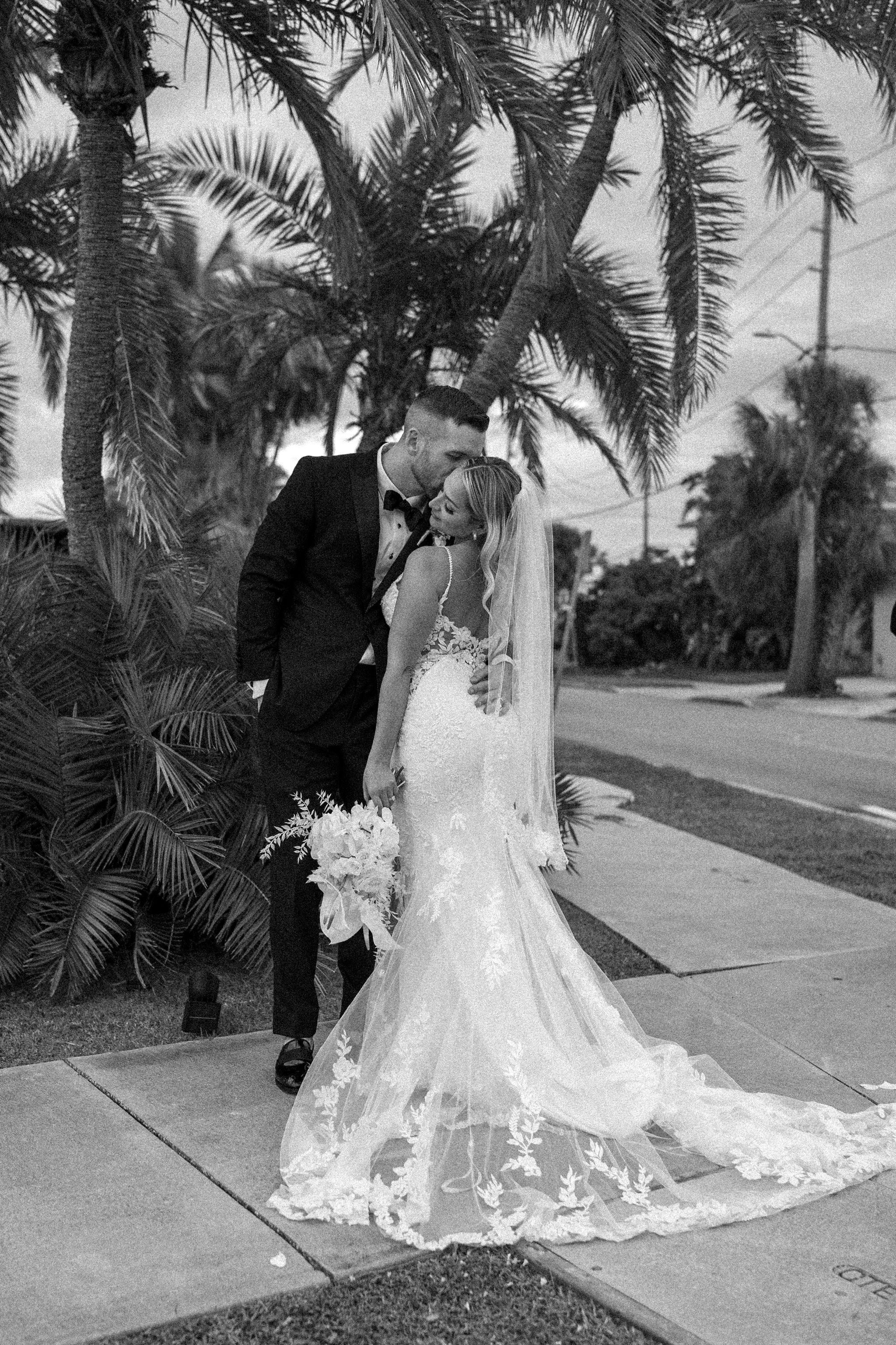 Wedding couple poses beneath tropical palm trees in elegant black and white photography.