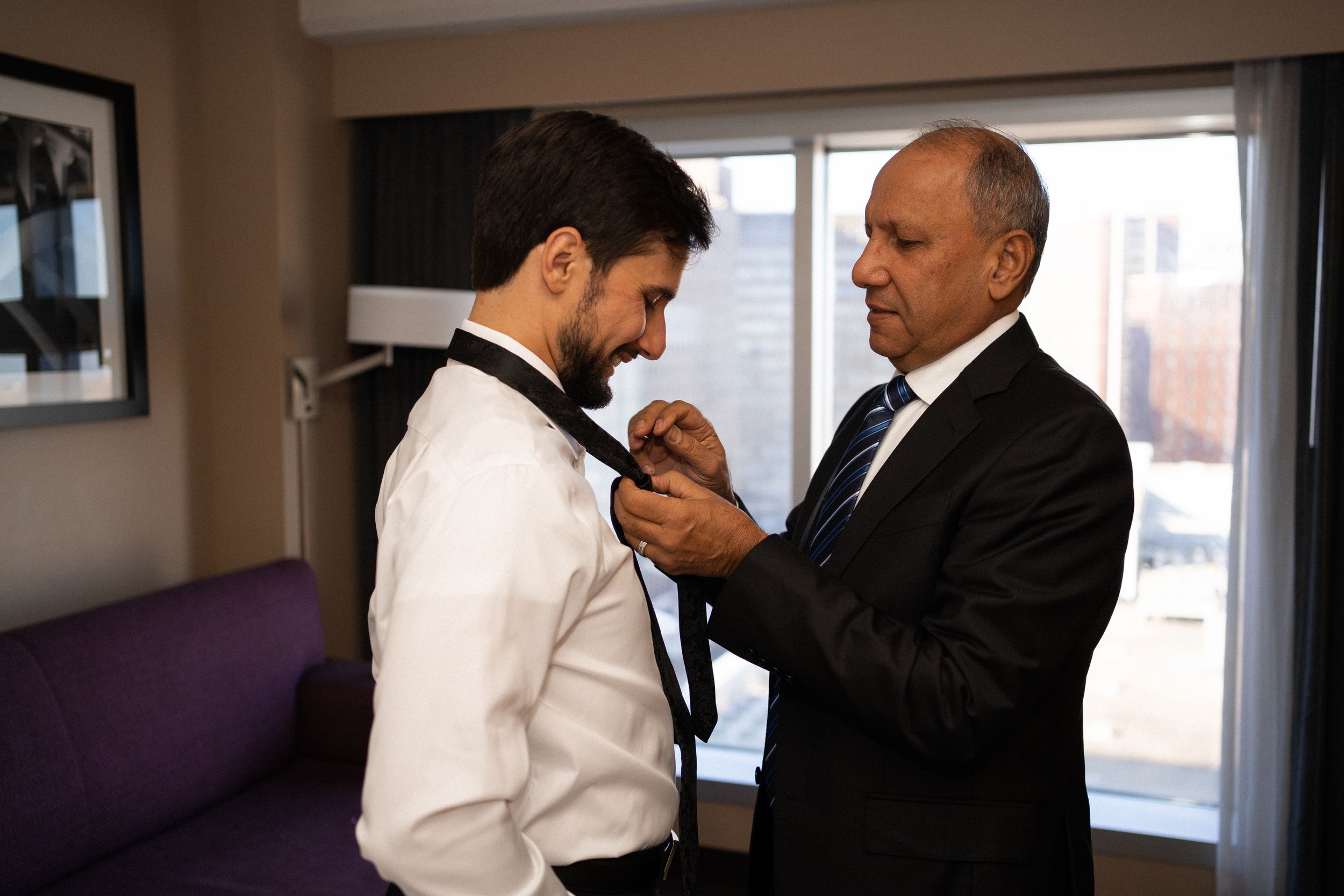 Father helping adjust groom's tie before wedding ceremony.