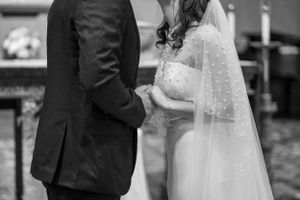 Close-up black and white image of bride and groom holding hands during wedding ceremony.