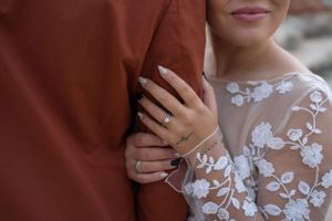 Close-up of hands with wedding ring against floral lace dress detail.