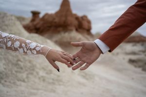 Two hands reaching to hold each other against a desert rock formation background.