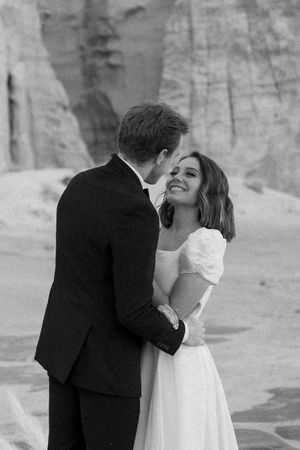 Black and white portrait of a couple sharing an intimate moment against desert cliffs.