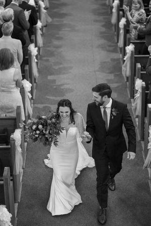 Newlyweds walking down church aisle while wedding guests look on from pews.