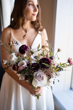 Beautiful bridal bouquet with purple and lavender roses held against white wedding dress.