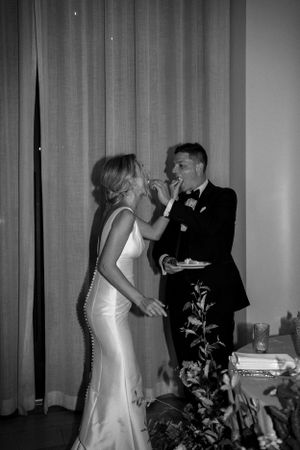 Newlyweds share cake during their wedding reception in black and white photograph.