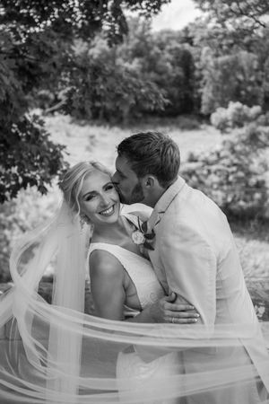 Romantic black and white portrait of newlyweds embracing outdoors with flowing veil.