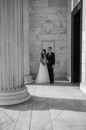 Newlyweds pose elegantly between marble columns at a classic architectural venue.