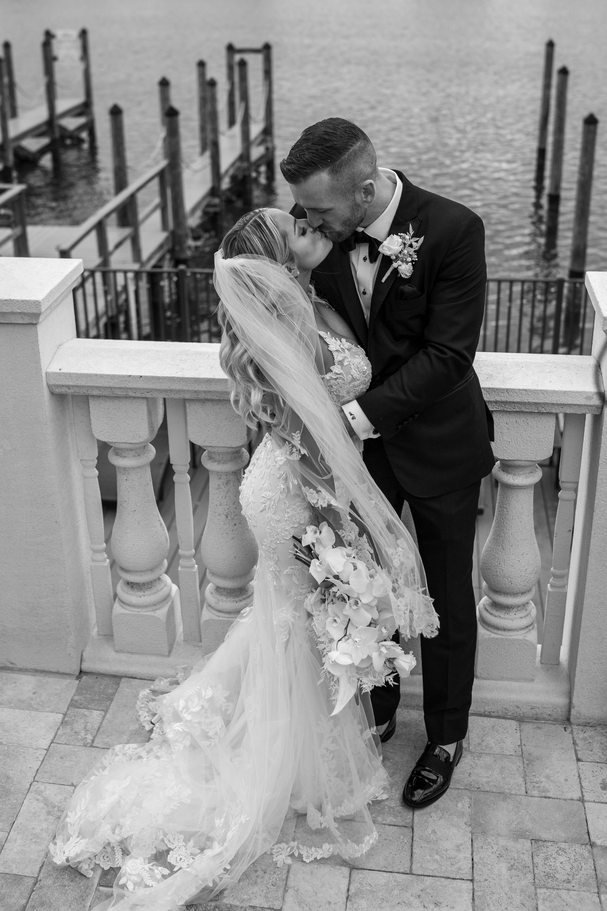 Romantic moment between newlyweds on a waterfront balcony with ornate railings.
