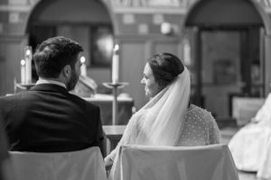 Black and white photo of newlyweds sitting side by side during church ceremony.