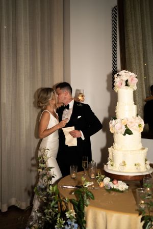 Couple shares intimate moment next to elegant tiered wedding cake decorated with pink flowers.