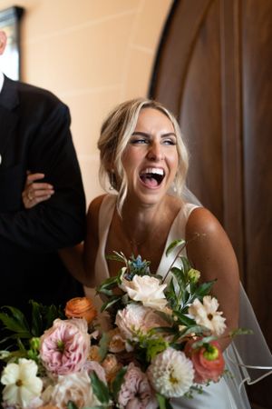 Candid moment of joyful bride laughing while holding elegant floral bouquet.