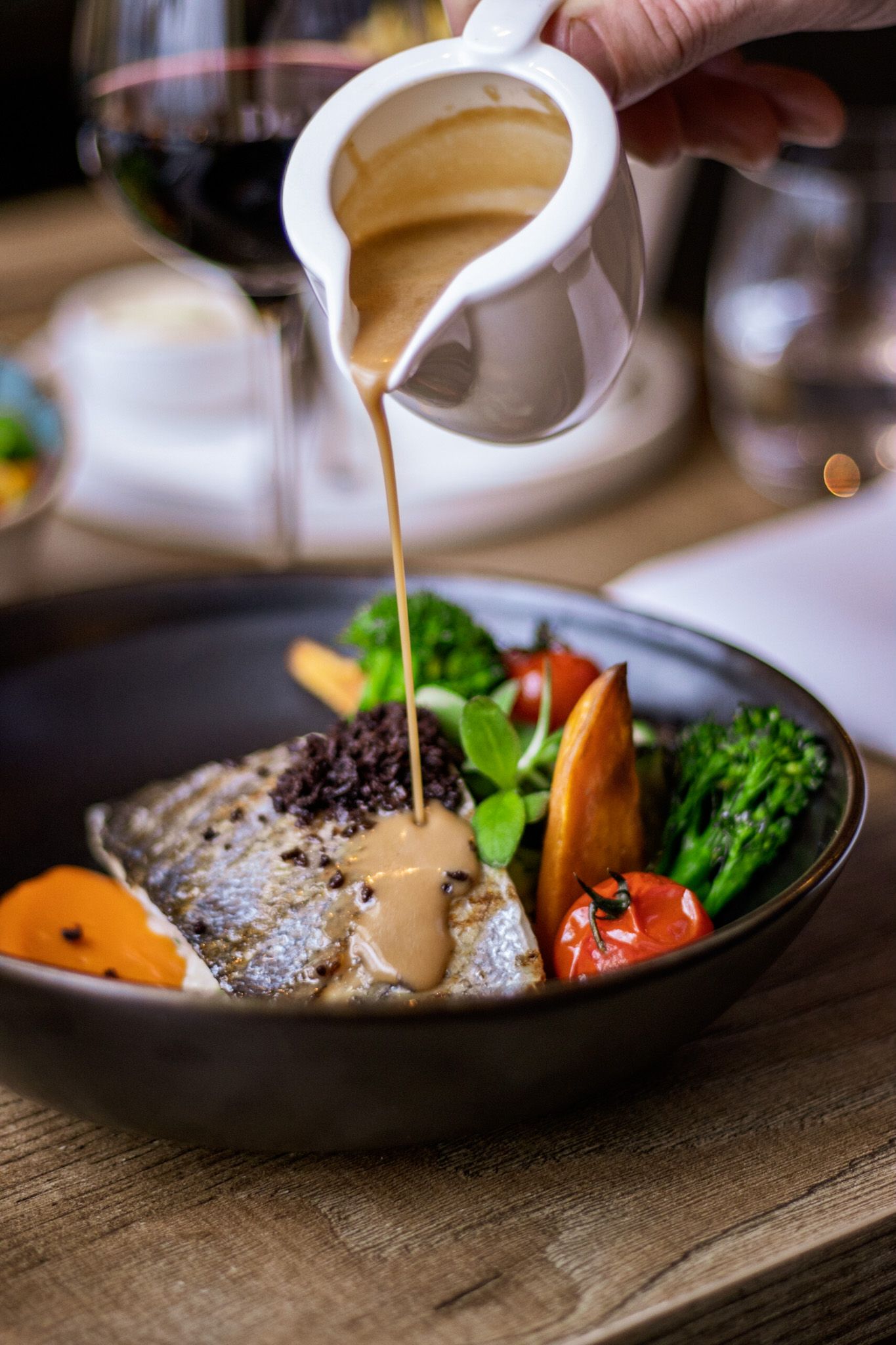 Een bruine saus wordt geschonken over een visgerecht uit een wit kannetje, perfect voor culinaire fotografie