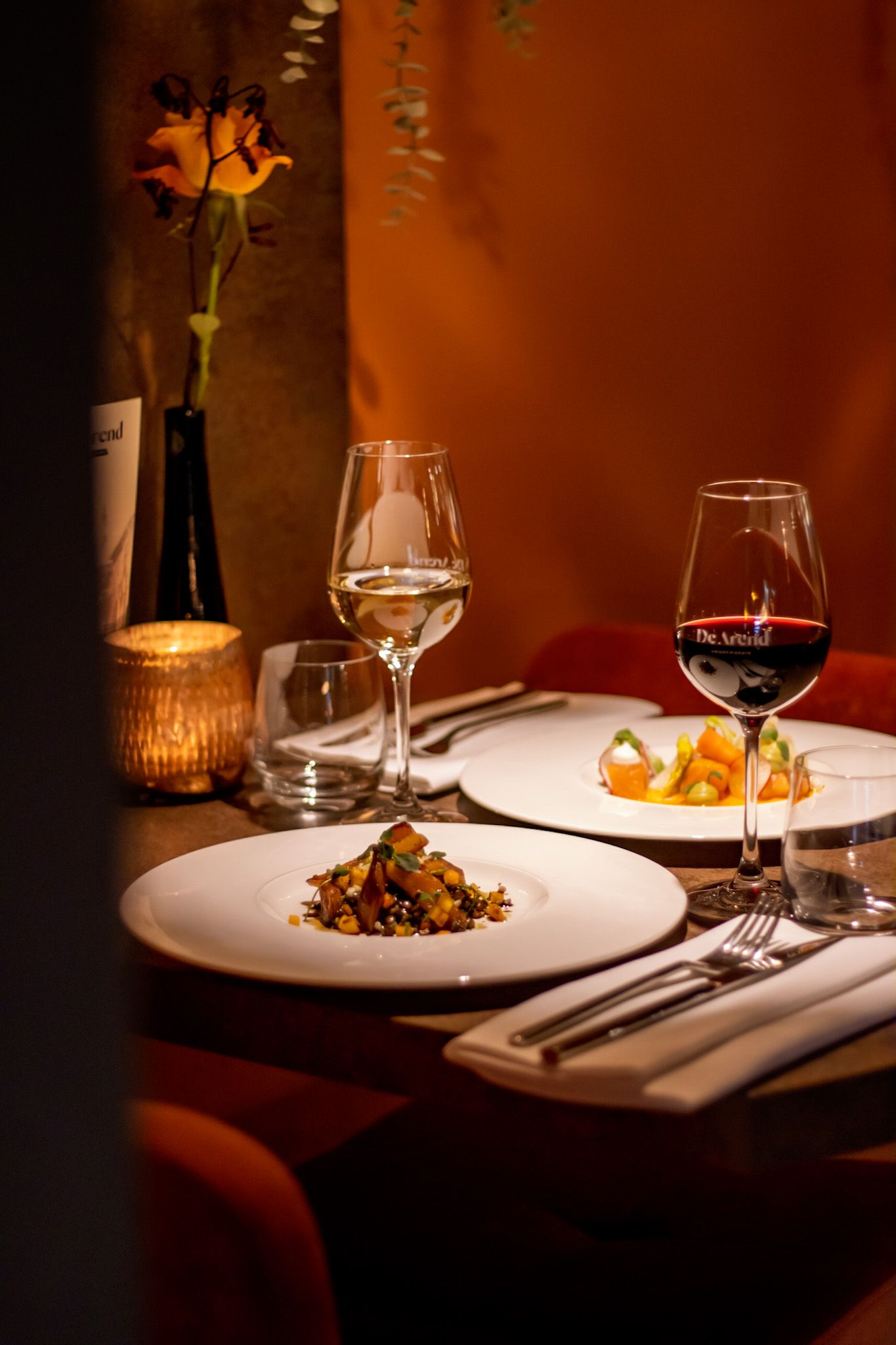Restauranttafel met voorgerechten, volle wijnglazen en sfeervolle bruin-rode achtergrond, perfect voor culinaire fotografie.