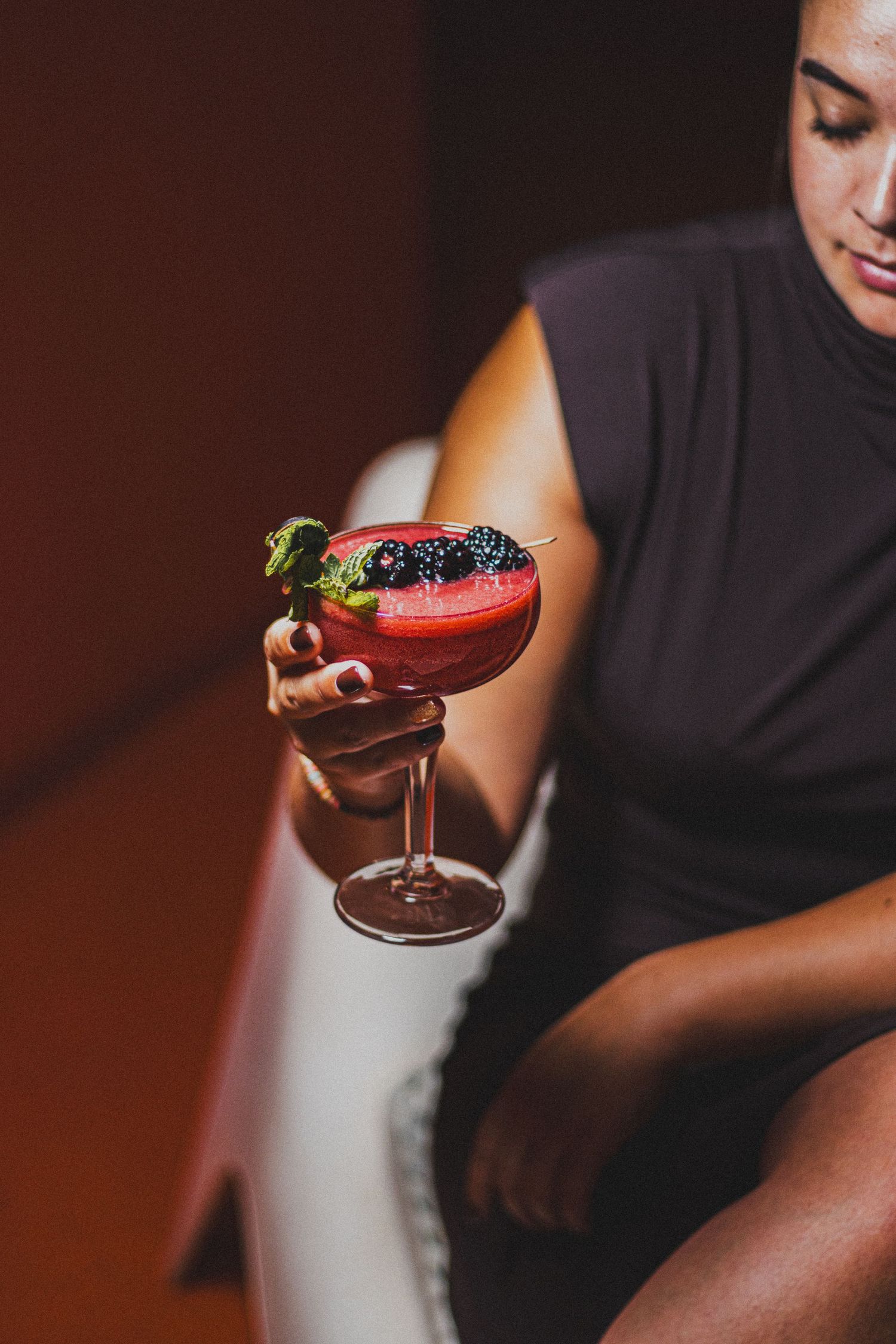 Vrouw met elegante rode cocktail gegarneerd met bessen, gefotografeerd in warme sfeerverlichting.