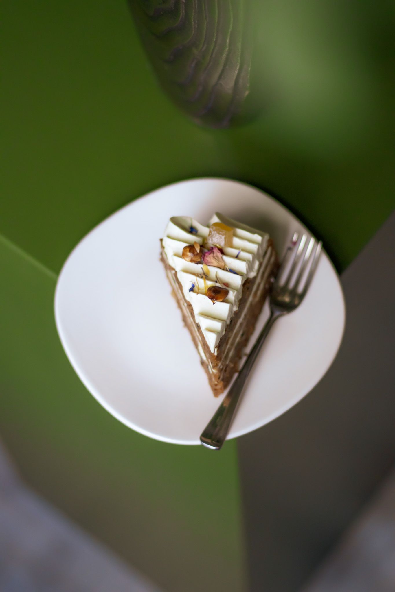 een carrot cake op een wit bordje met een vorkje en een groene achtergrond.