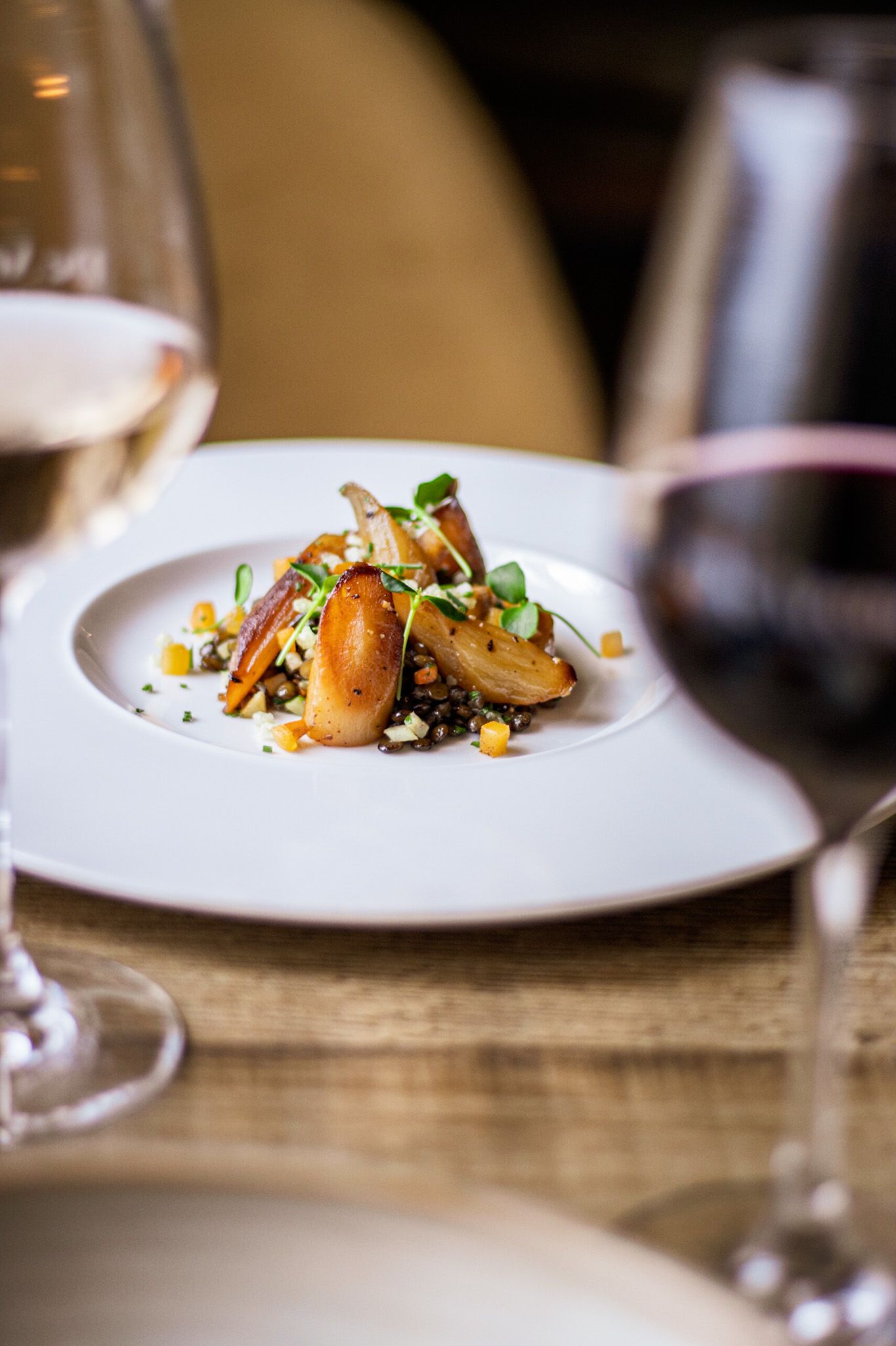 Scherpte op een gerecht met witte en rode wijnglazen in de voorgrond, ideaal voor gastronomische fotografie.