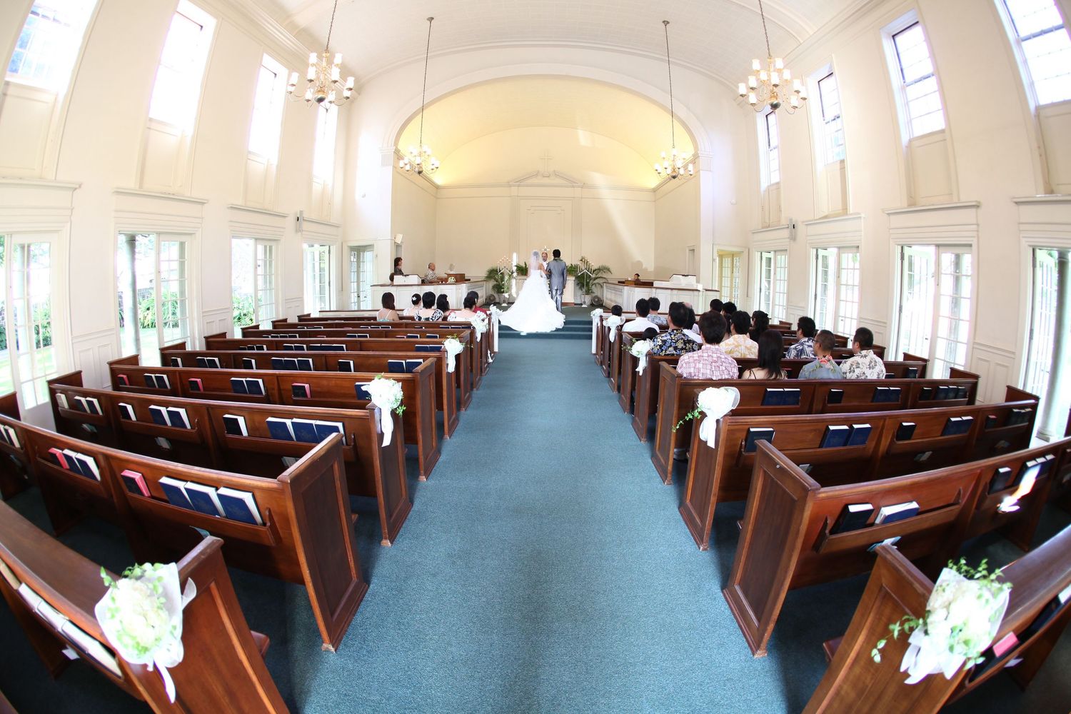 Elegant church wedding ceremony with wooden pews, blue carpet aisle, and bright arched windows.