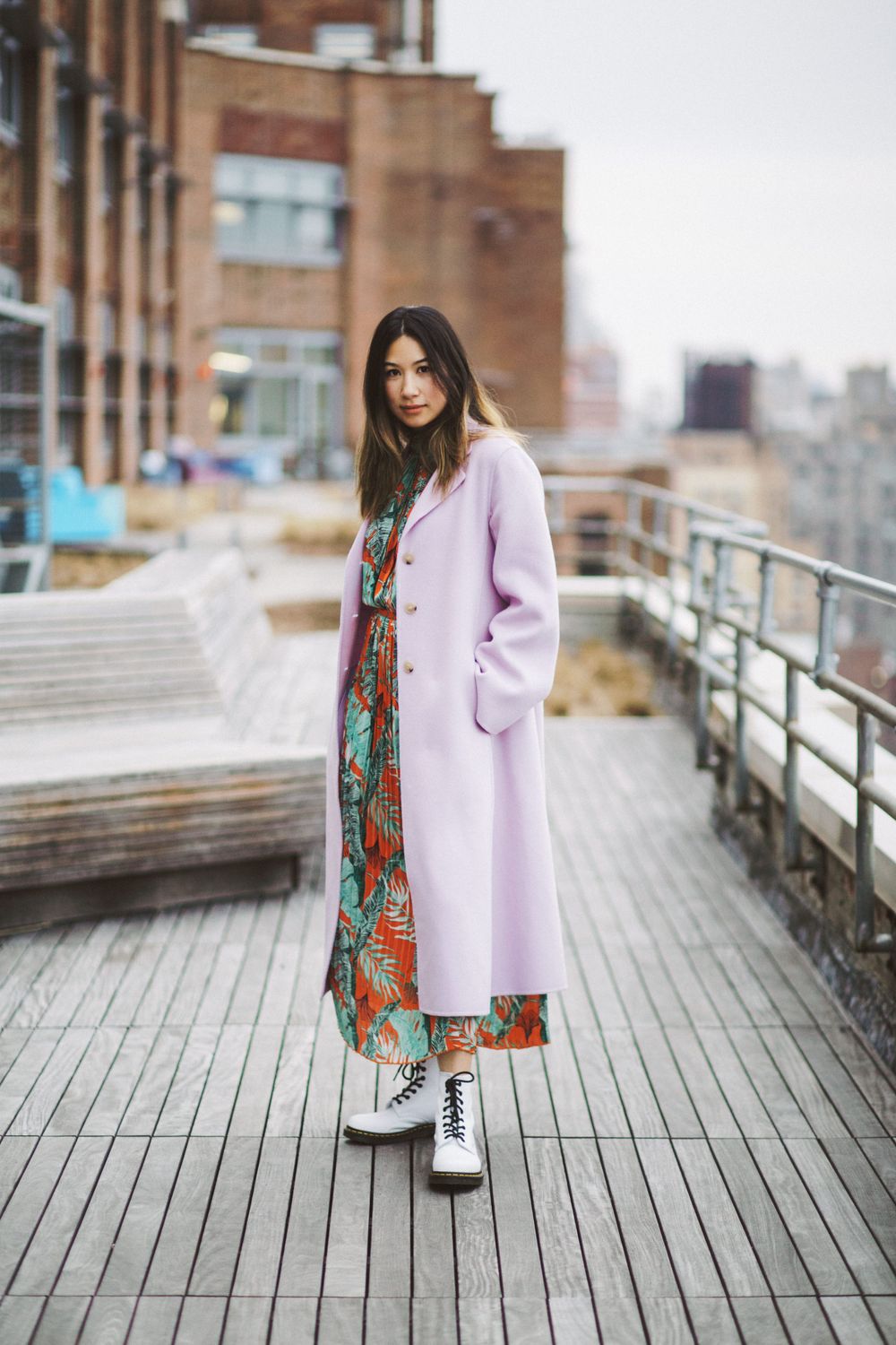 Street style photo of person in lilac coat and floral dress on rooftop boardwalk.