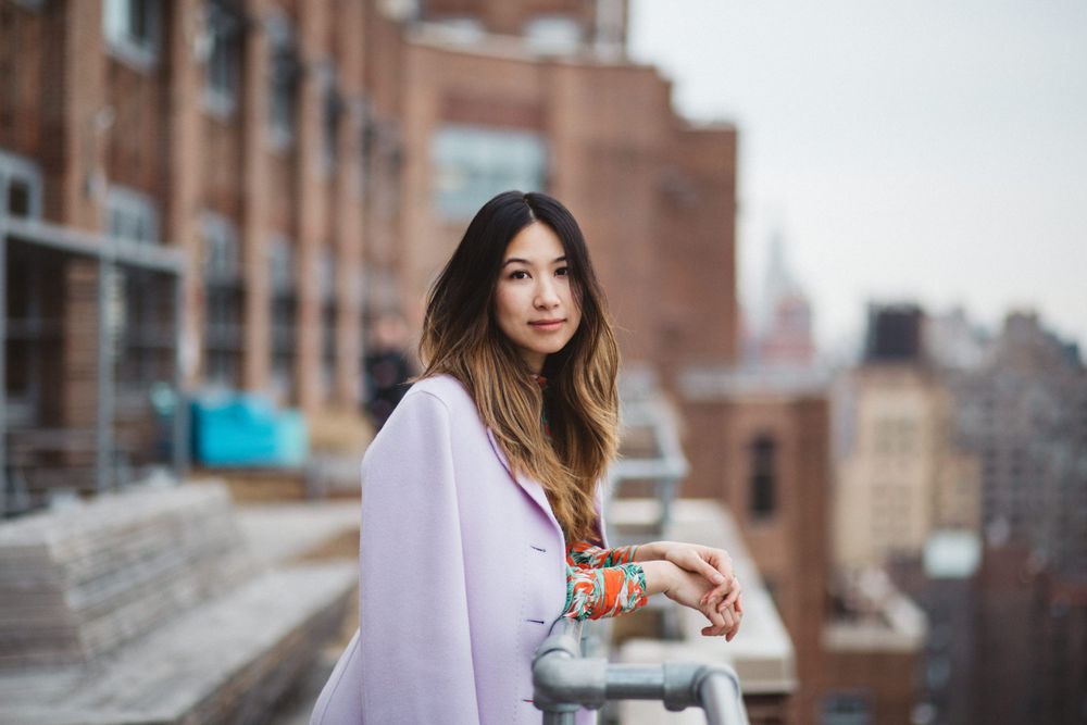 Urban fashion portrait with person in lilac coat against city backdrop.