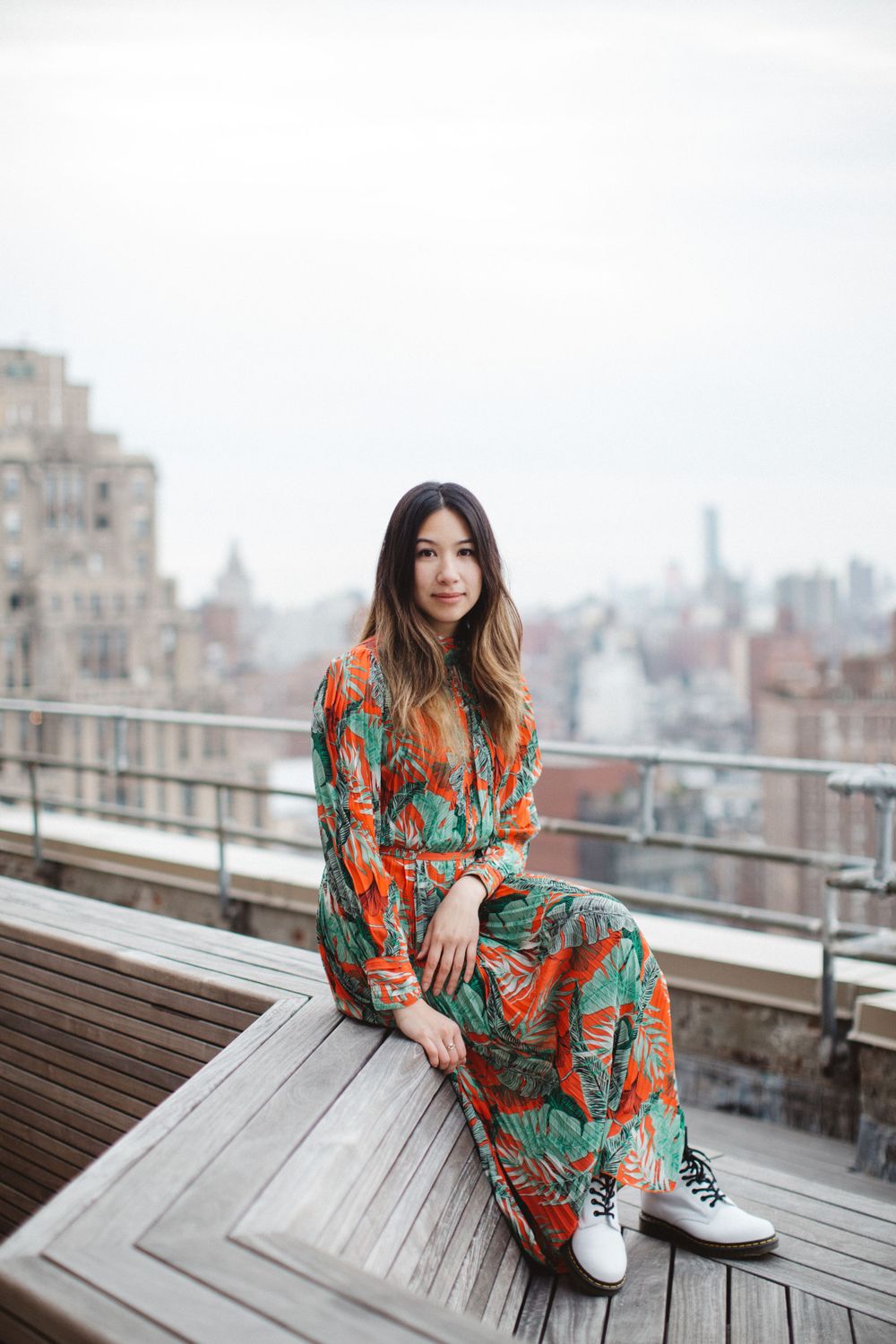 Colorful orange and teal floral maxi dress styled with white sneakers on a rooftop deck overlooking a city skyline.