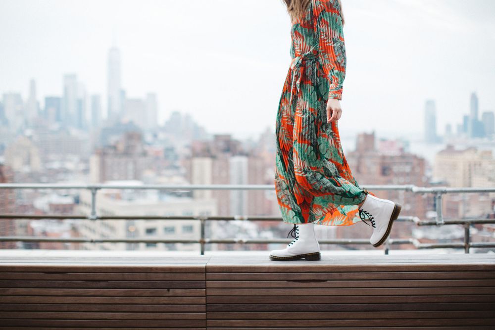 White sneakers paired with flowing printed maxi dress against urban skyline backdrop.