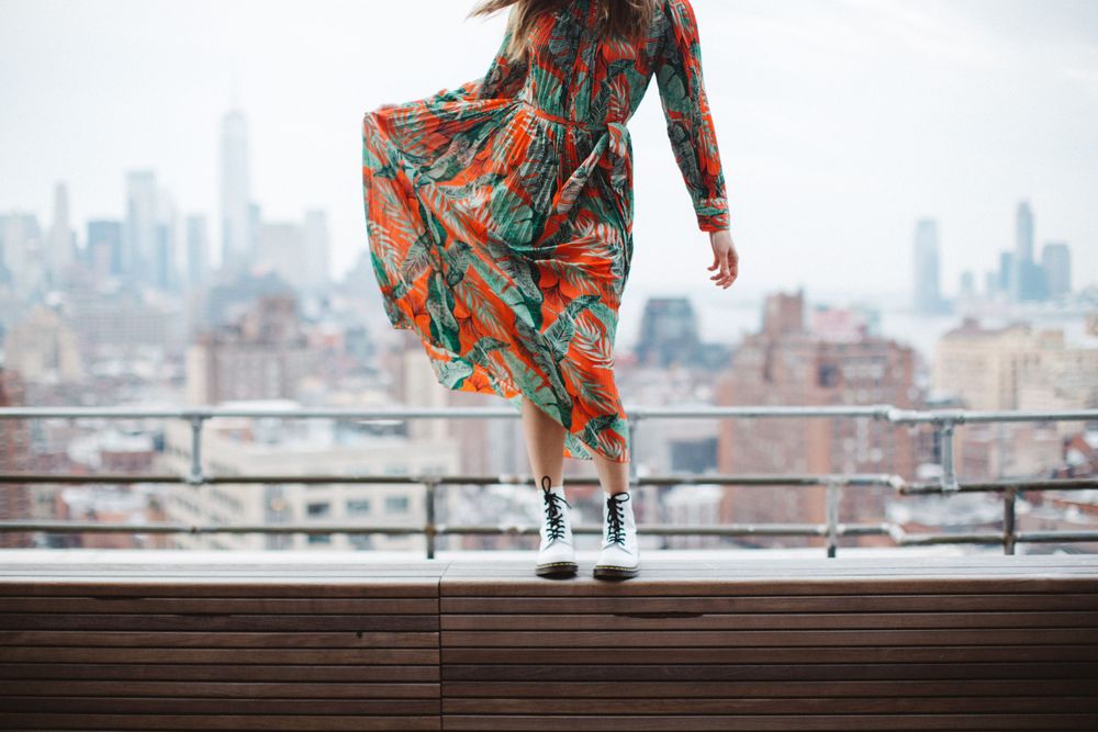 Orange and teal floral dress swaying in wind on rooftop with city vista.