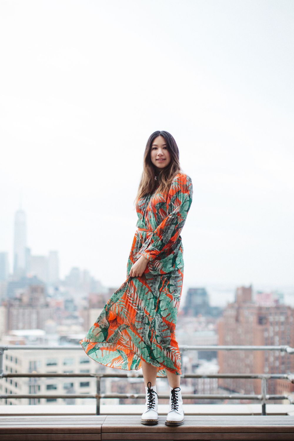 Vibrant floral maxi dress and white sneakers on wooden deck with city views.