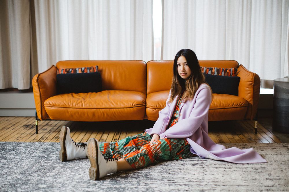 Interior scene with orange leather couch and pink throw blanket against white curtains.