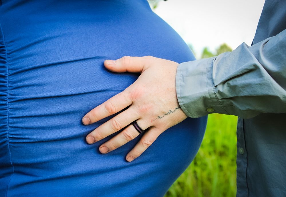 Close-up image for a Maternity photoshoot of a man's ring hand on a woman's pregnant belly.