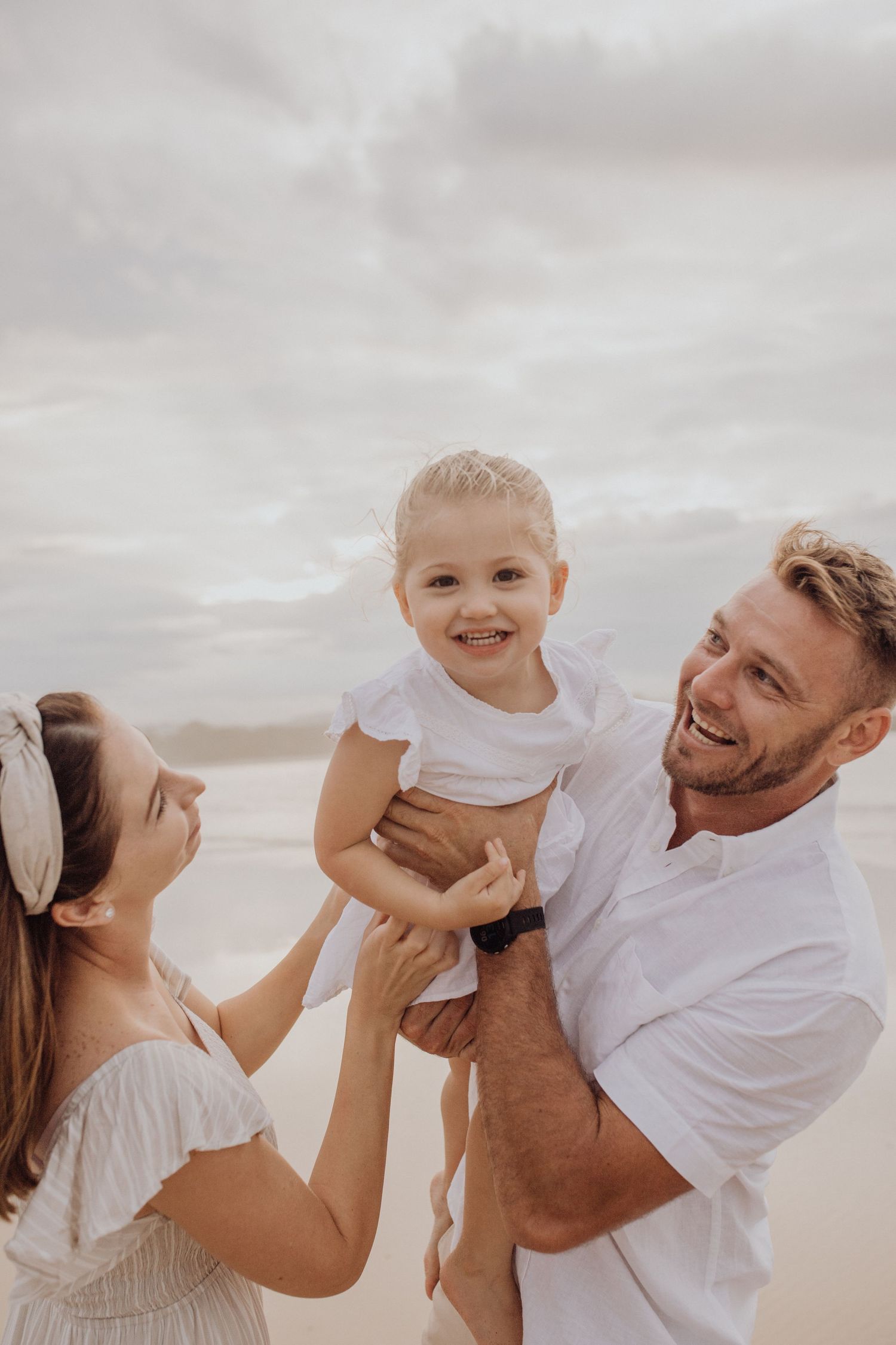 Father holding his young daughter up in the air playing with ocean in background