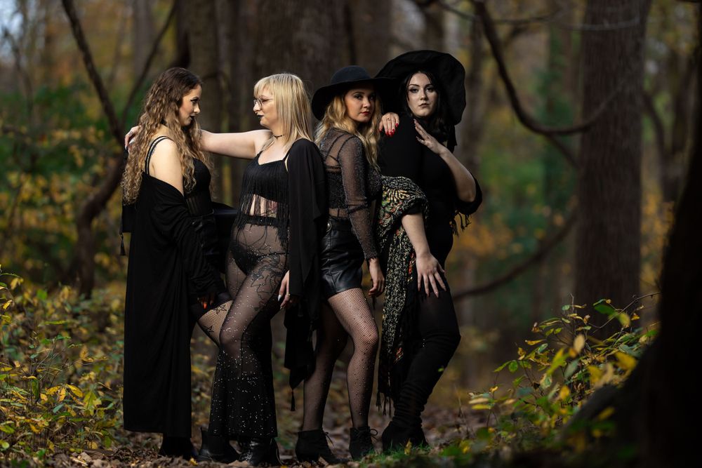 A group photo in dark attire posing dramatically in an autumn forest setting.