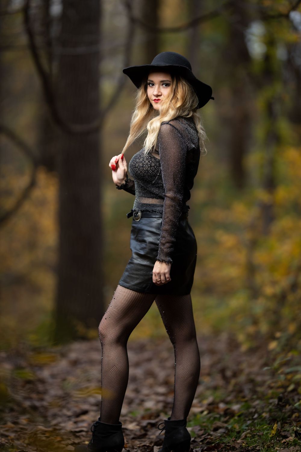 Gothic inspired outfit with wide brim hat and mesh top against blurred woodland backdrop.