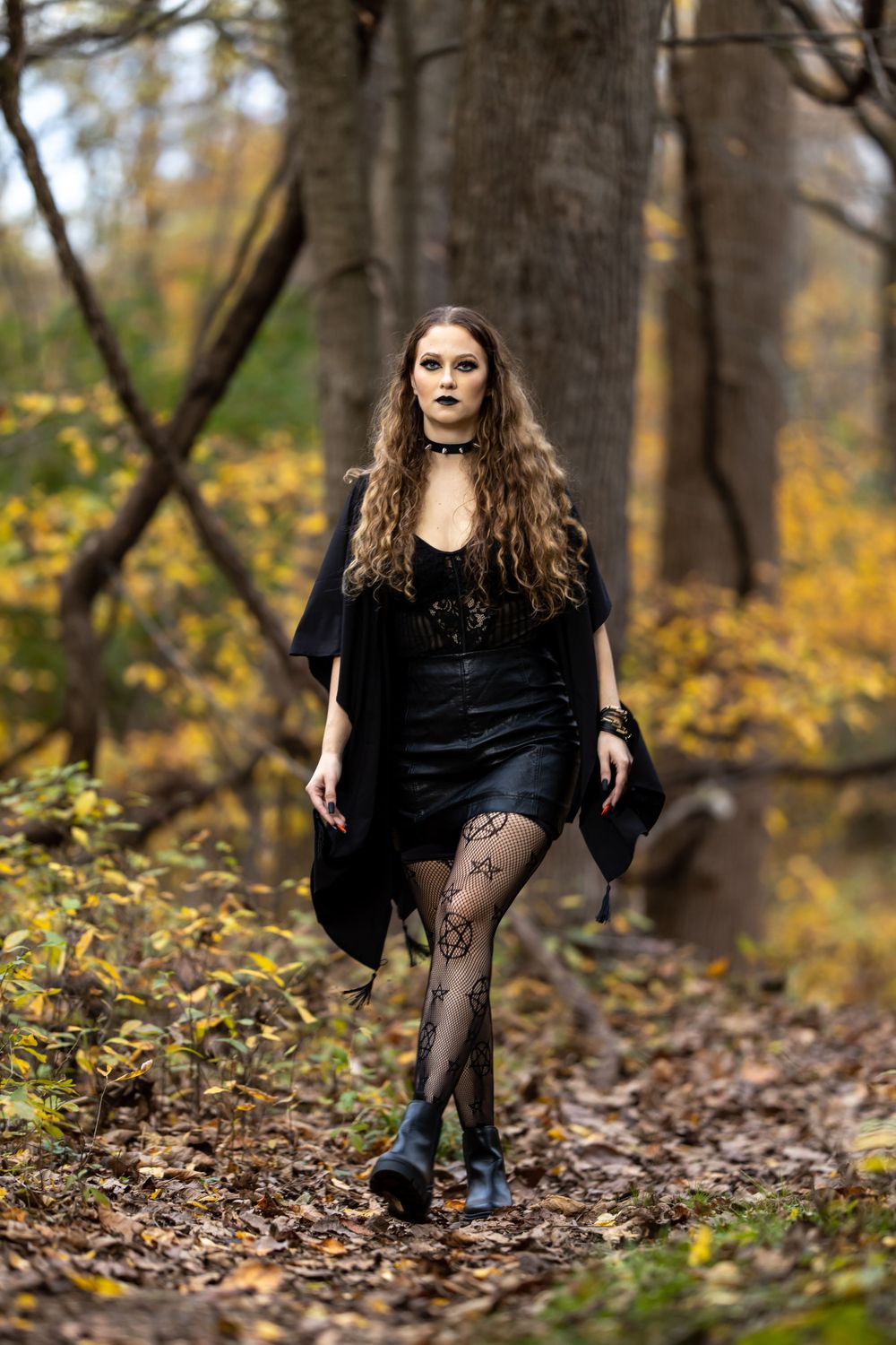 Autumn forest fashion portrait featuring long black coat and patterned tights on woodland path.