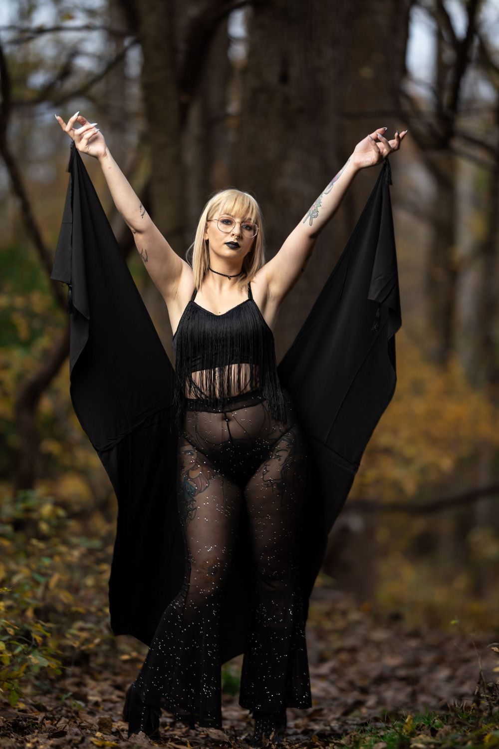 Dramatic fashion pose with flowing black fabric against moody forest backdrop.