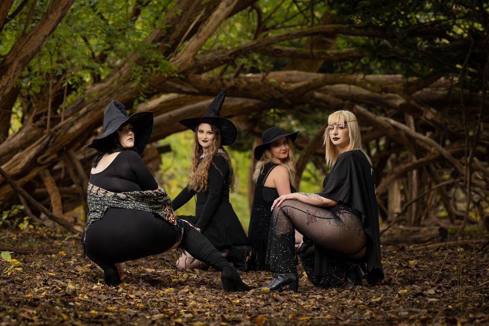 Group photo of models in dark attire posed together on fallen logs in a forest setting.